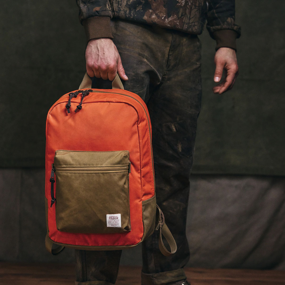 Filson Surveyor 25L Backpack Dark Tan/Flame, gedragen aan het handvat